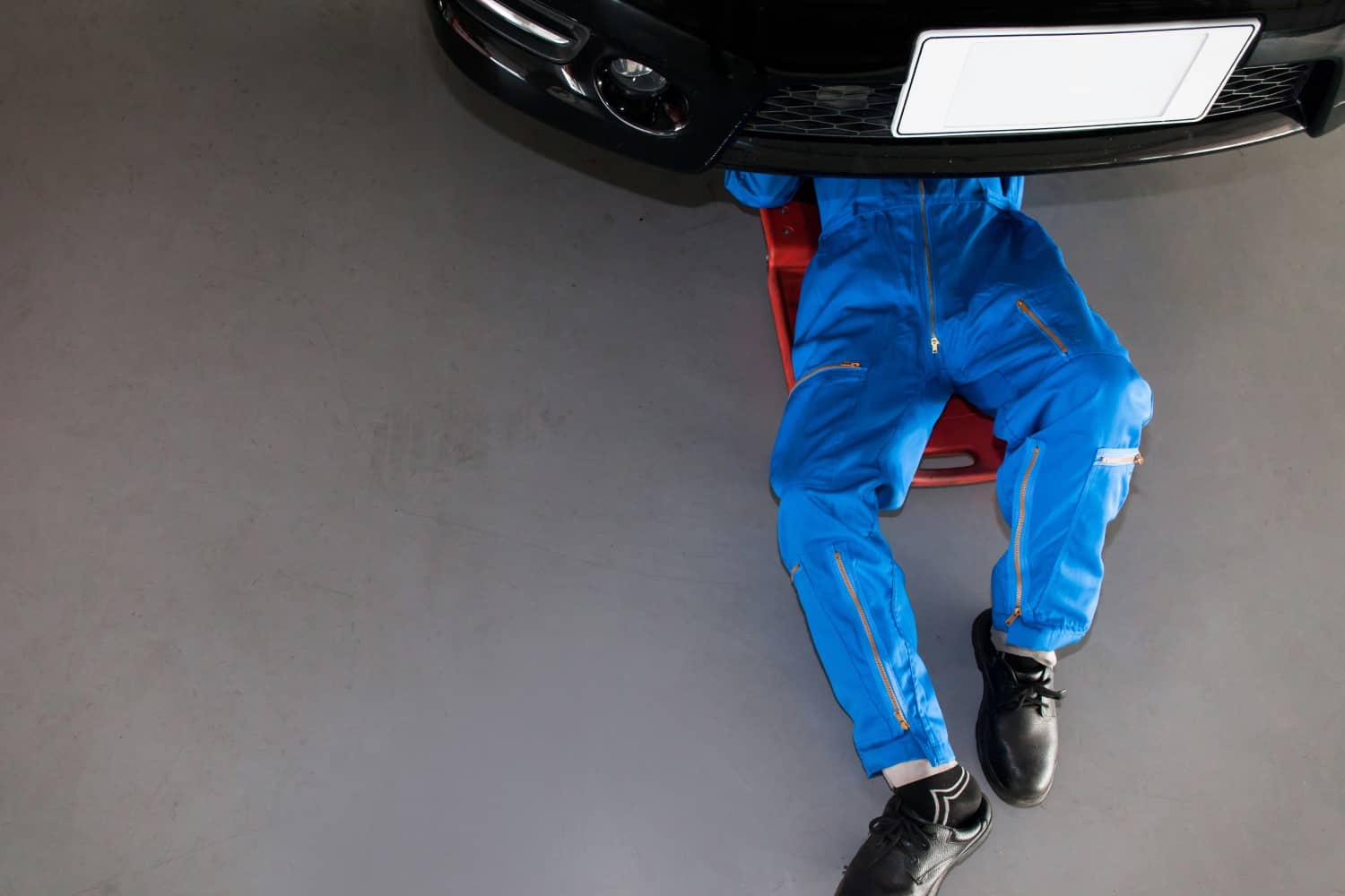 stock-photo-mechanic-in-blue-uniform-lying-down-and-working-under-car-at-the-garage-404805970-min